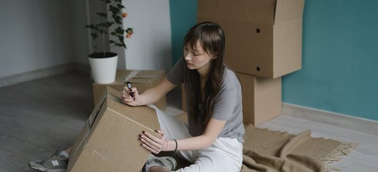 A woman labeling a cardboard box while decluttering