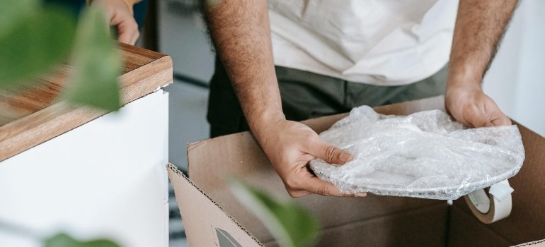 A person packing a plate in a bubble wrap.