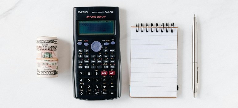 A calculator next to a notebook and a stack of money.