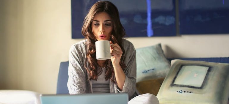 A young woman drinking coffee and using a computer to find out why storage solutions are essential for young couples.