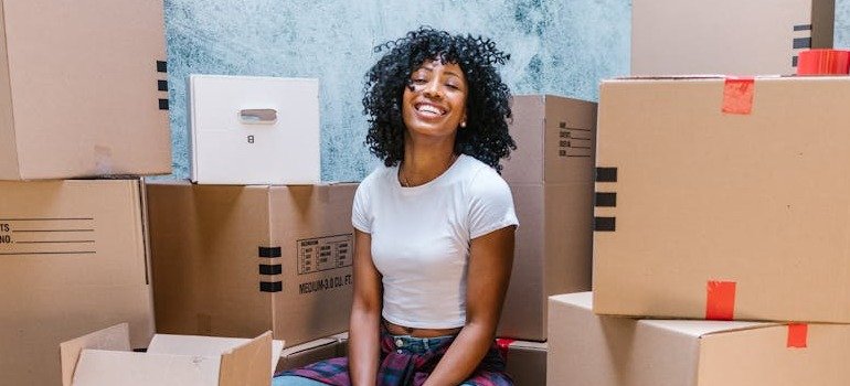A girl smiling among moving boxes before taking them to the storage Clinton Hill offers.