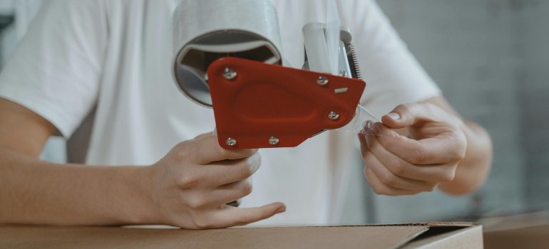 A man packing boxes and securing them with a tape.