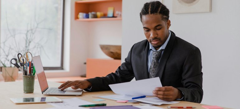 A person in a suit carefully reviewing documents and working on a laptop, representing the decision-making process when choosing a storage location.