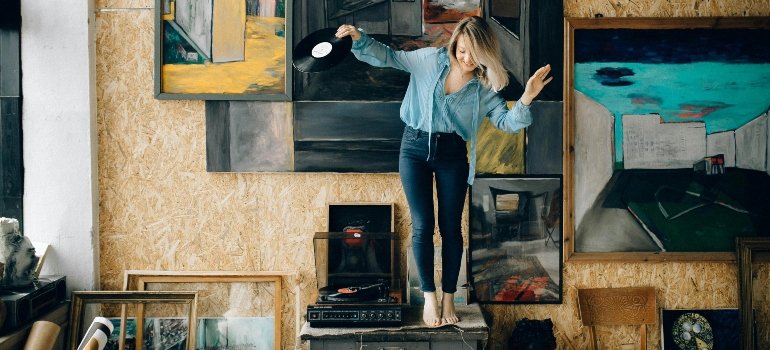 Woman handling vinyl record among her art collection, showcasing the need for climate-controlled storage to protect delicate artwork and media.