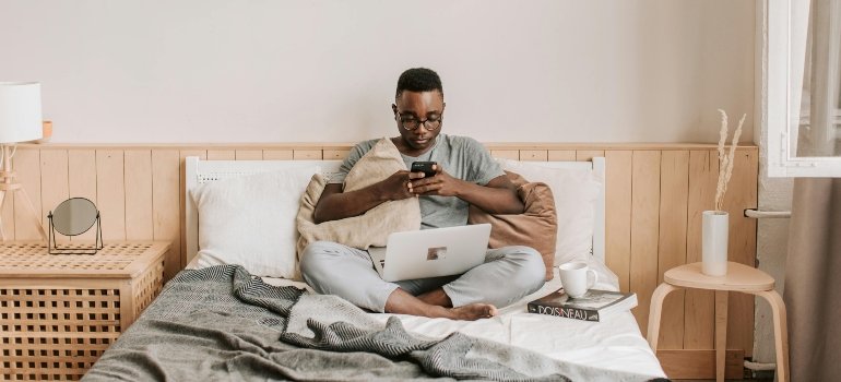 A man on his bed doing remote work after learning about the challenges of securing a job before moving to Queens.