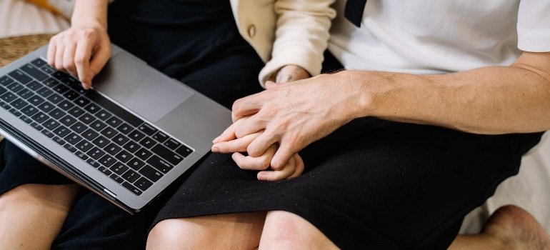 A couple is holding hands and using a laptop.