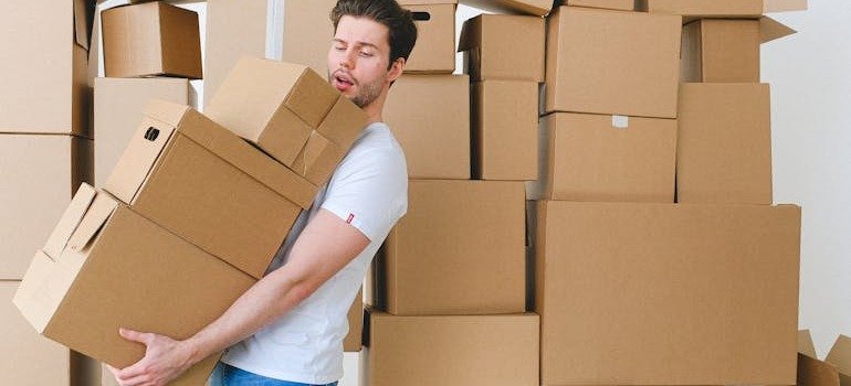 A young man carrying a pile of boxes after finding an apartment in Brooklyn as a student.