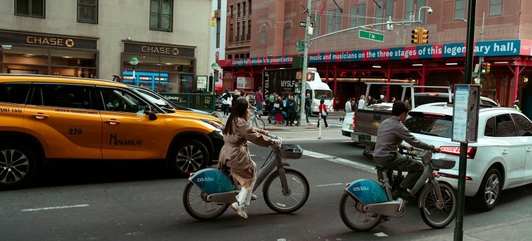 A couple is riding bikes on the streets while thinking about storing different types of vehicles in NYC.
