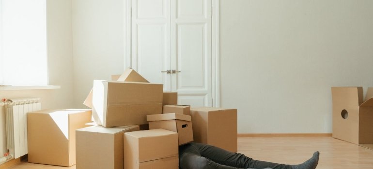 A man lying on the floor under a pile of cardboard boxes because he doesn't know that storage is essential when downsizing.
