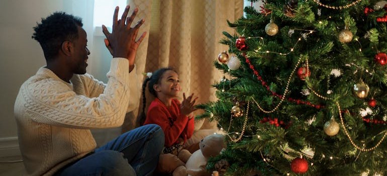 A child and a dad having fun next to the Christmas tree.