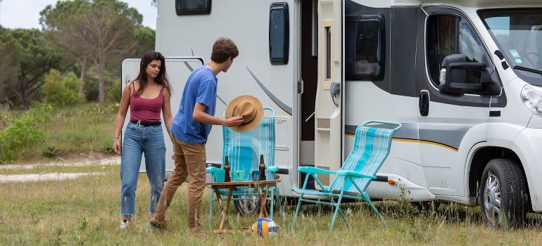 A man and a woman are standing beside a camper.