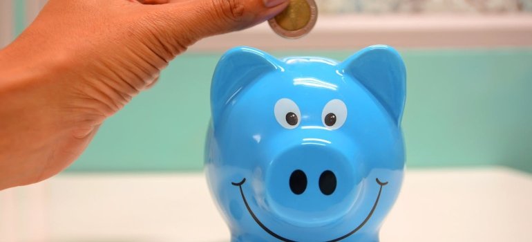 A hand putting a coin into a piggy bank to save for right size storage unit.