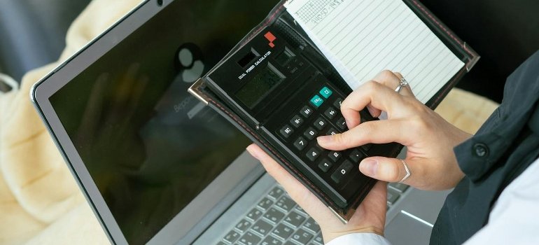 A woman is using both a calculator and laptop.