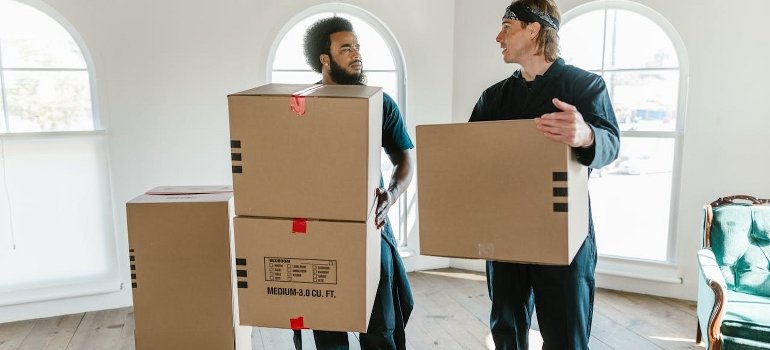 Men are carrying cardboard boxes while having a conversation on the ways to store winter essentials and holiday items.