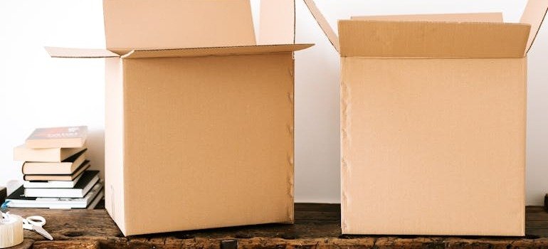 Two open boxes on a table with books and other items beside them.