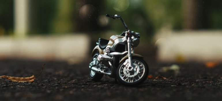 Tiny motorcycle resting on a road surface with green trees in the backdrop.