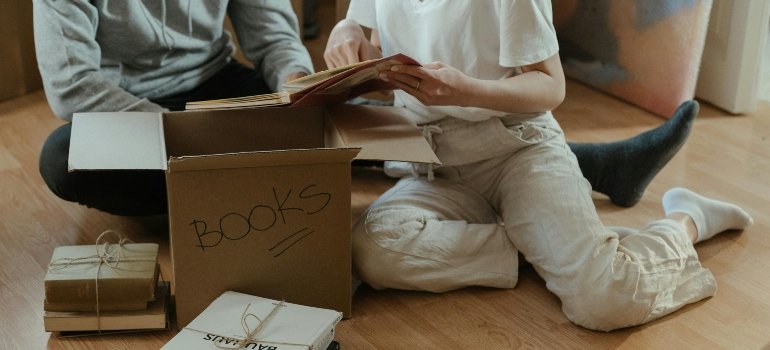 Two people packing books into a box, carefully preparing items for secure storage after comparing storage costs in Manhattan and NYC’s surrounding area.