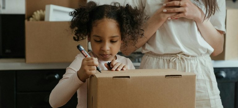 A young girl writing on a moving box while her family prepares for relocation using small storage units in the Bronx.
