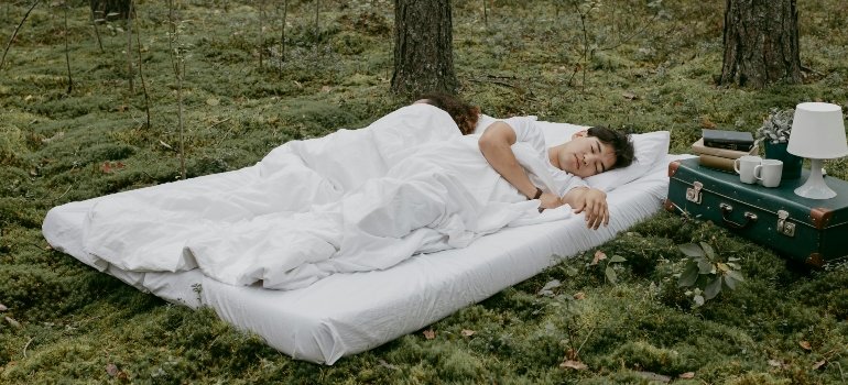 A young man sleeping on a mattress outdoors.