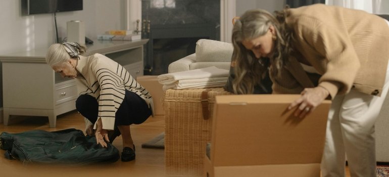 Two elderly women packing household items into boxes after exploring storage in NYC for different uses.