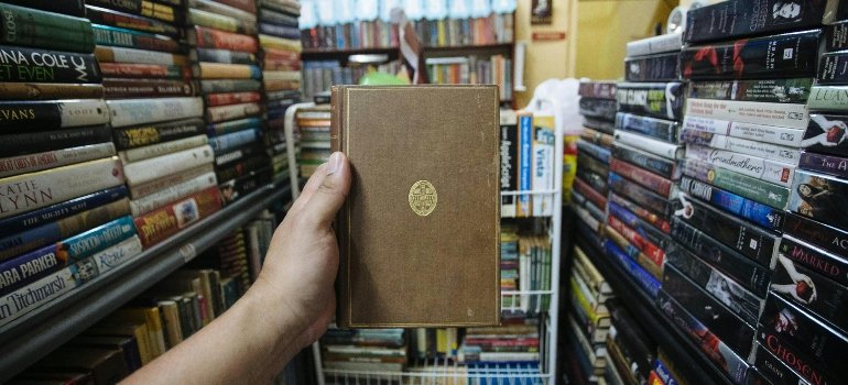 A hand holding a vintage book surrounded by stacked shelves — a collector’s dream, made easier by renting storage in Brooklyn for book collection.