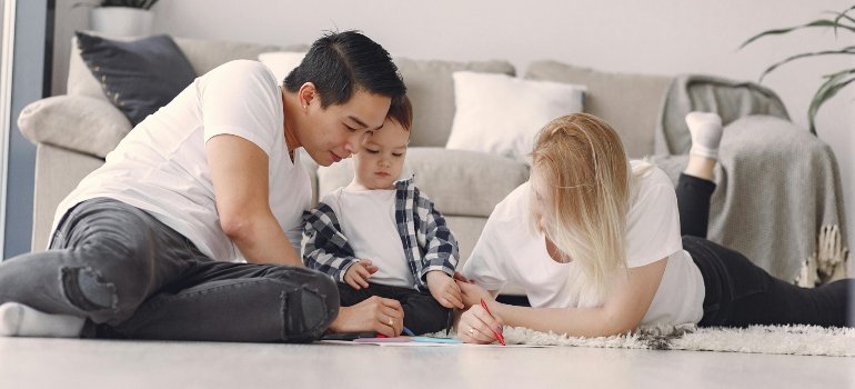 A young family enjoying creative activities on a soft carpet in a bright living room after storing mattresses and sofas.