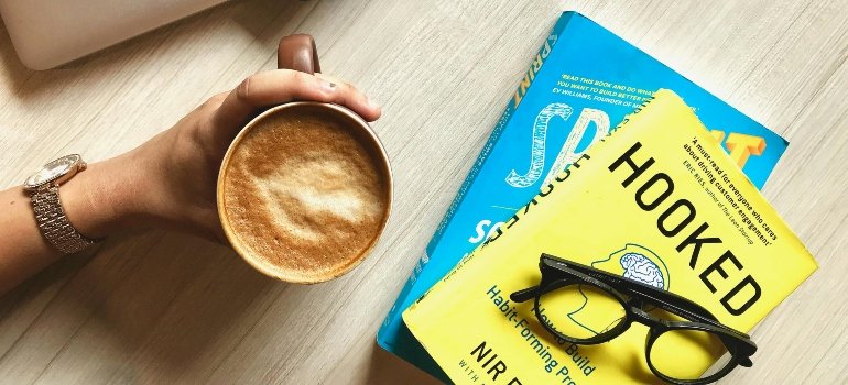 A hand holding a cup of coffee next to books 'Hooked' and 'Sprint' on a wooden table.
