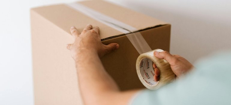 A person taping up a cardboard box, preparing for storage or moving.