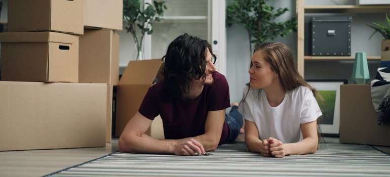 Couple lying on a rug surrounded by moving boxes, preparing for a new chapter in their NYC home by dicsuccing storage in NYC for different uses.