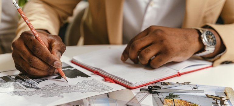Close-up of a person in a tan blazer writing and drawing plans for a construction assignment.