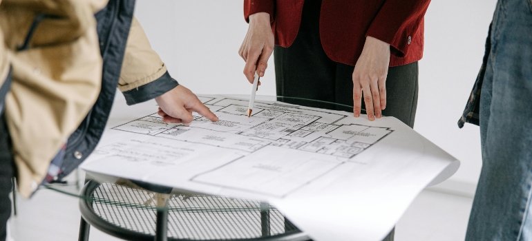Hands pointing at a detailed floor plan on a small table, preparing for a building job.