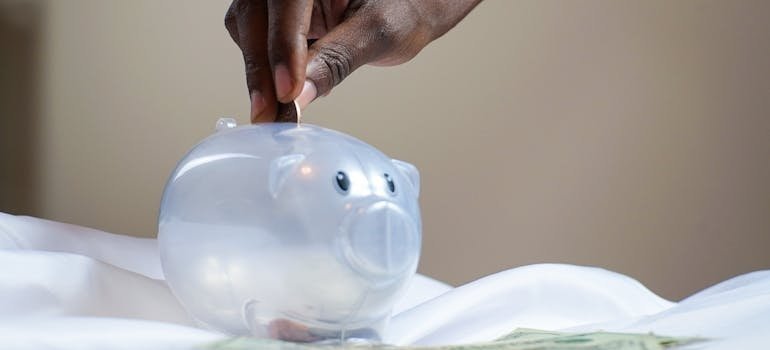 Person putting a coin in a piggy bank, which symbolizes saving money as the result of the fact that NYC residents choose moving and storage services together.