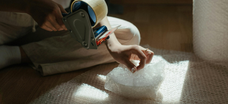 A person using bubble wrap to pack some items as you should do when you pack and store your dorm room over break .