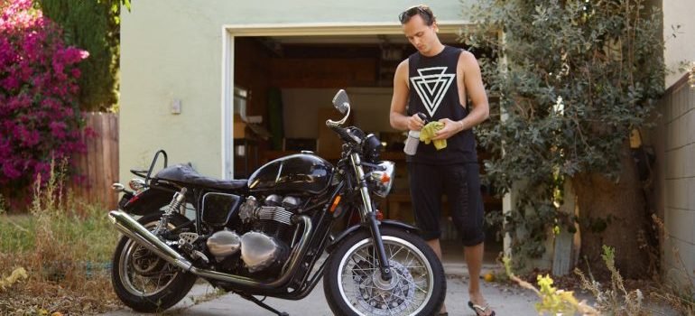 A Man in Black Sleeveless Shirt Cleaning a Motorcycle and thinking about Protecting your motorcycle from theft and damage in storage