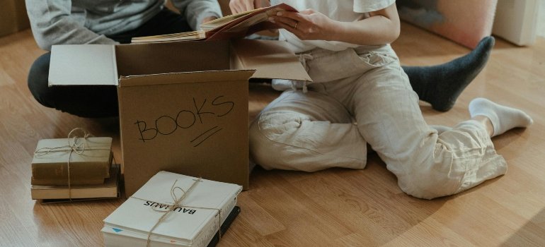 A couple carefully packing novels in carboard boxes,which are among the essential moving supplies for your move.