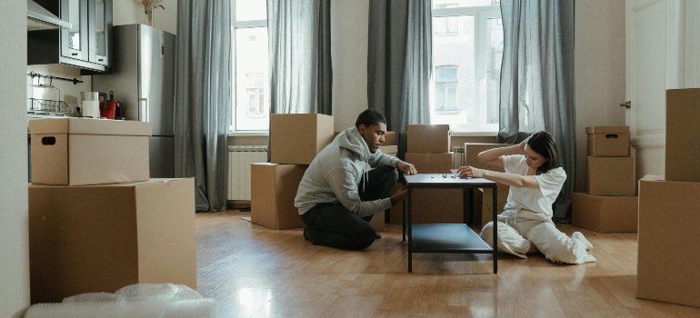 A pair disassembling a table and piles of packed cardboard boxes.