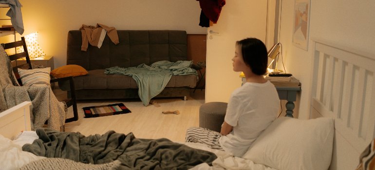 A woman sitting in a messy room before discovering why storing items away is better than cluttering your home.