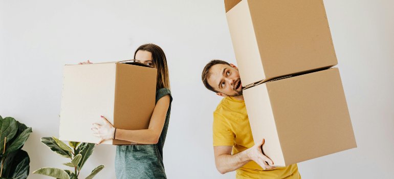Two people holding cardboard boxes after learning that storing items away is better than cluttering your home