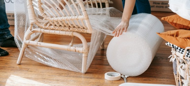 A woman wrapping a chair into bubble wrap and demonstrating how to pack furniture while moving.