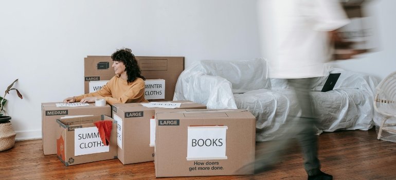 A person surrounded by large moving boxes labeled with seasons and books, showing a new way to store your belongings at home.