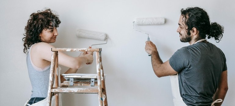 A woman and a man applying paint on a white wall with rollers.