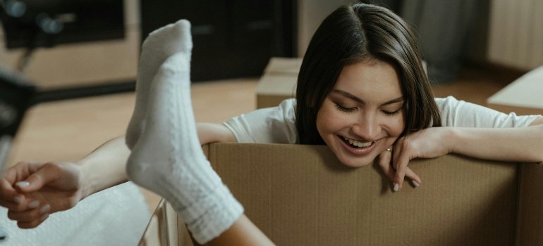 Young woman laughing while looking at a child sitting inside a cardboard box during a home move.