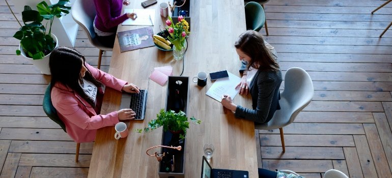 Overhead view of people typing on laptops at a long wooden table.