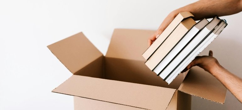 Hands placing books in a box after looking at an important checklist while choosing storage services.