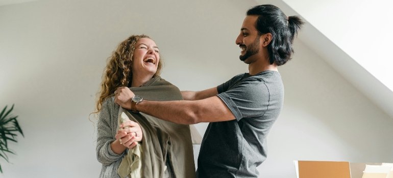 Happy couple laughing together while unpacking clothes in their new home.