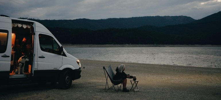 Van parked by a tranquil lake at dusk with a person enjoying coffee; an ideal moment before you prepare your RV for self-storage.