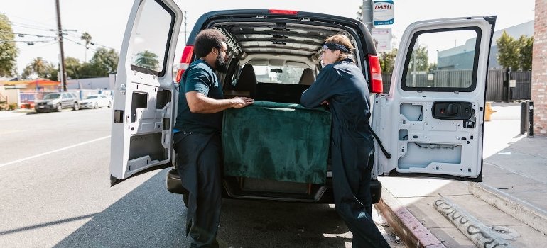 Two men are loading a green couch onto a moving van.