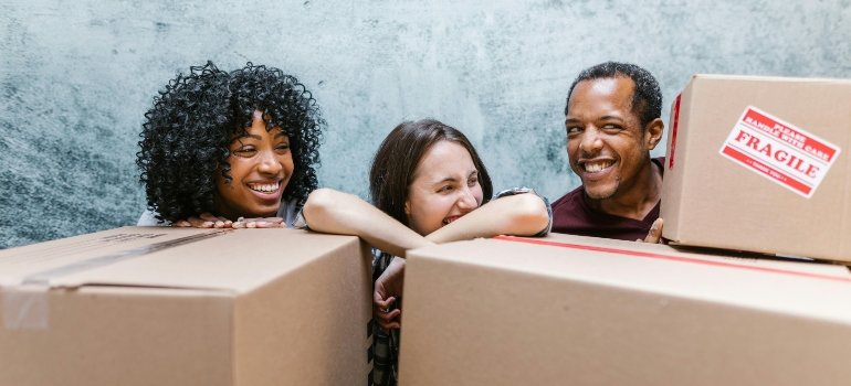 Three cheerful friends laughing around moving boxes once they find out when you need a self storage unit.