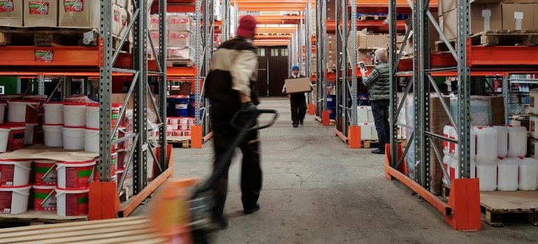 A busy warehouse with employees sorting and moving goods using pallet jacks and manual carts.