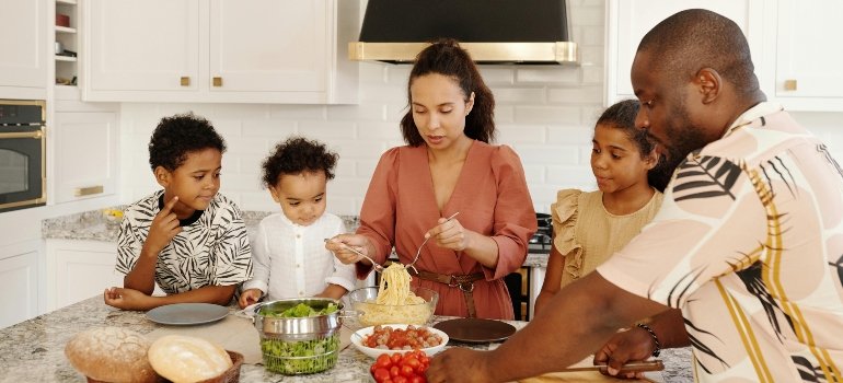 A mother and father cooking together with their children gathered around a kitchen counter.
